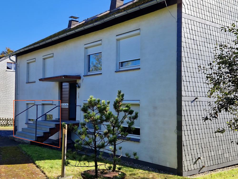 Das Gebäude der Ferienwohnung bei sonnigem Wetter, umgeben von Grün und Blumen.