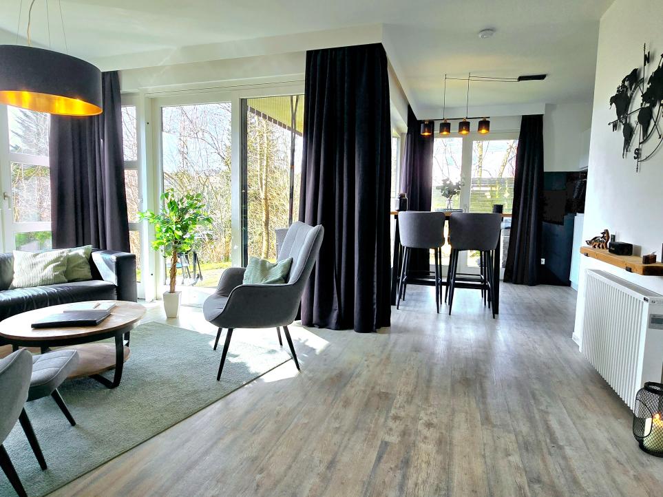Wohnzimmer mit großem Fenster, Pflanzen und modernem Mobiliar in der Ferienwohnung.