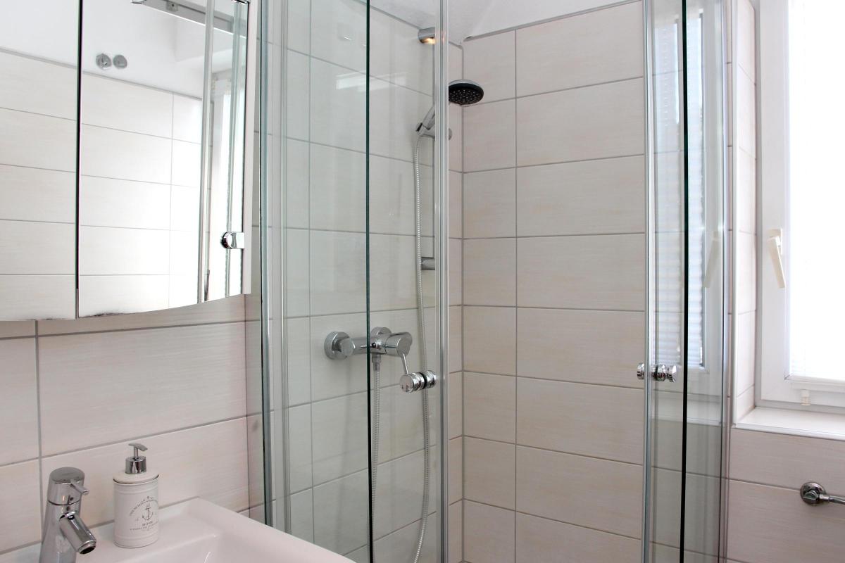 Badezimmer mit Dusche, Waschbecken und Spiegel in der Ferienwohnung Möhnesee.